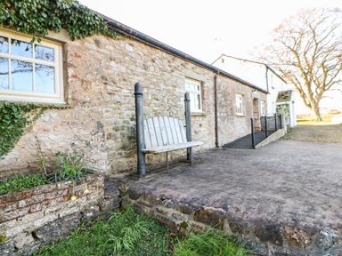 An outdoor area with a stone wall cottage wooden bench and a small garden bed at Cherry Tree Cottage Soulby near Kirkby Stephen