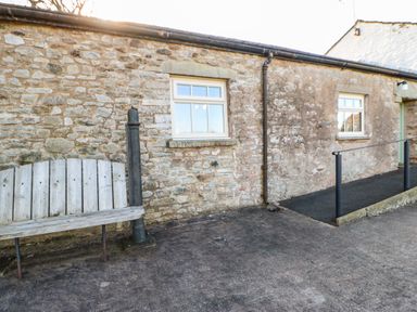 A stone wall with two windows a wooden bench and a ramp with metal railings at Cherry Tree Cottage Soulby near Kirkby Stephen