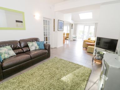 A living room with a leather sofa and green rug next to a TV and dining area at Mountain View in Conwy