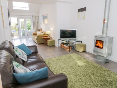 A living room with two sofas a television on a stand a wood stove and glass doors leading outside at Mountain View in Conwy