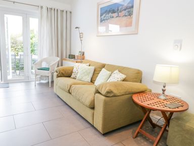 A living room with a green sofa white chair wooden side table and glass doors at Mountain View in Conwy