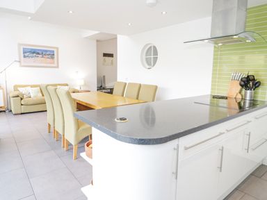 A kitchen with a black countertop and stove next to a dining table with six chairs and a sofa in the background at Mountain View in Conwy