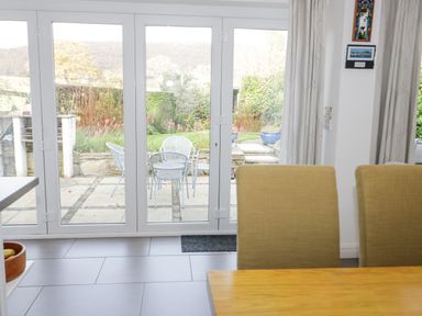 A dining area with beige chairs next to glass doors opening to a garden patio at Mountain View in Conwy