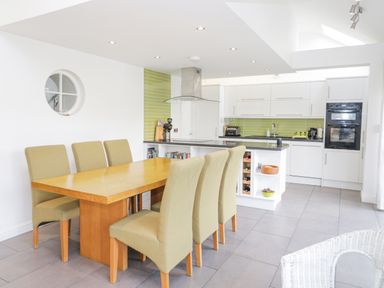 A kitchen and dining area with a wooden table and six green chairs at Mountain View in Conwy