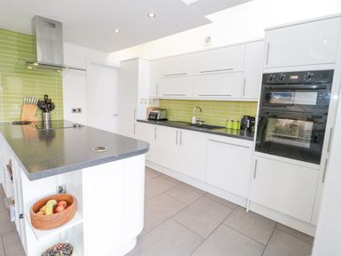 A kitchen with white cabinets a green tiled backsplash and a gray countertop at Mountain View in Conwy