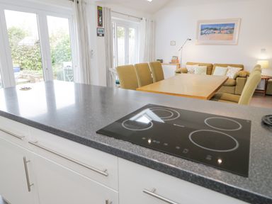 A kitchen counter with an electric stove and a dining area with chairs and a sofa at Mountain View in Conwy