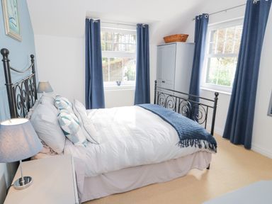 A bedroom with a metal bed frame, white bedding, blue pillows, blue curtains, a small wardrobe with a basket on top, and a bedside lamp at Mountain View in Conwy