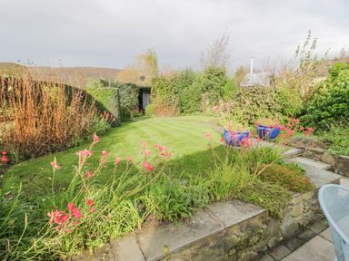 A garden with a lawn surrounded by plants flowers stone walls and a shed in the background at Mountain View in Conwy