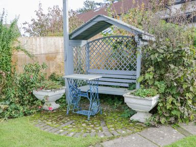 A garden seating area with a covered wooden bench and a small table with plants in planters at Mountain View in Conwy