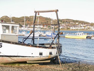 A boat on the shore near a body of water with other boats and houses on hills in the background at Mountain View in Conwy
