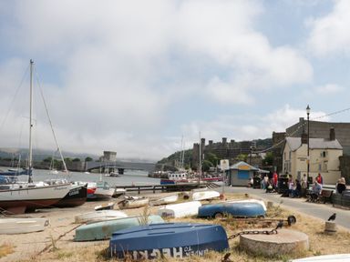 A harbor with small boats pulled ashore people sitting on benches near a building with a sign Liverpool Arms and a castle in the background at Mountain View in Conwy