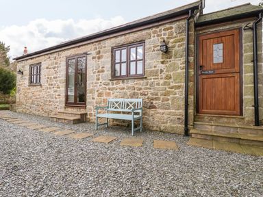 Exterior view of a stone building with wooden door and windows and a bench on a gravel path at Brocks Barn Sweetshouse near Lostwithiel