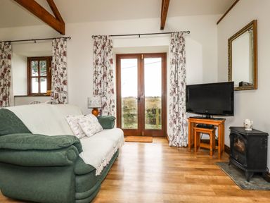 A living room with green sofa wooden floor tv and floral curtains at Brocks Barn Sweetshouse near Lostwithiel