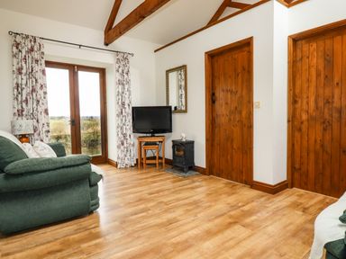 A living room with wooden doors a television and patterned curtains at Brocks Barn in Sweetshouse near Lostwithiel