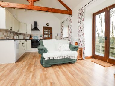 An open plan kitchen and living area with a green sofa wooden beams and glass doors at Brocks Barn Sweetshouse near Lostwithiel