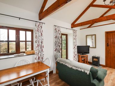 A living room with wooden beams dining table chairs sofa television and a small stove at Brocks Barn Sweetshouse near Lostwithiel
