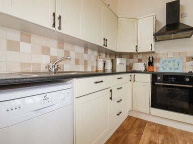 A kitchen with white cabinets a black countertop a dishwasher a sink an oven a toaster and kitchen utensils at Brocks Barn Sweetshouse near Lostwithiel