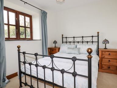 A bedroom with a black metal bed frame two wooden bedside tables with lamps and a window with blue curtains at Brocks Barn Sweetshouse near Lostwithiel