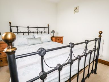 A bedroom with a metal framed bed a wooden nightstand and a lamp at Brocks Barn Sweetshouse near Lostwithiel