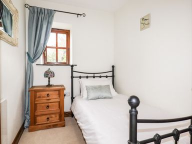 A small bedroom with a single bed a wooden nightstand with a lamp and a window with blue curtains at Brocks Barn Sweetshouse near Lostwithiel