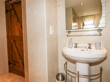 A bathroom with a pedestal sink a mirror wooden door and a metal trash bin at Brocks Barn Sweetshouse near Lostwithiel