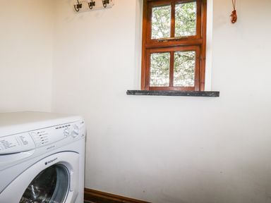 A laundry room with a washing machine under a wooden window at Brocks Barn Sweetshouse near Lostwithiel