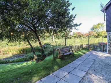 A garden with a tree string lights a wooden bench a paved pathway and a wooden fence at The Station Flat in St Newlyn East near Newquay