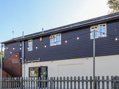 An exterior view of a two-story building with string lights hanging above a fenced area at The Station Flat in St Newlyn East near Newquay