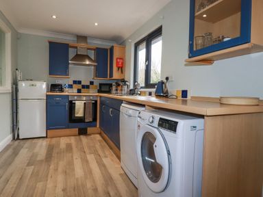 A kitchen with blue cabinets a washing machine dishwasher fridge and oven at The Station Flat in St Newlyn East near Newquay