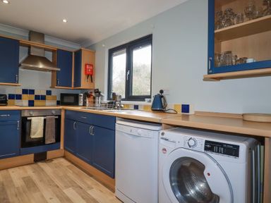 A kitchen with blue cabinets oven dishwasher washing machine and window at The Station Flat in St Newlyn East near Newquay
