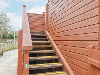 Wooden outdoor staircase with yellow safety strips alongside a wooden building at The Station Flat in St Newlyn East near Newquay