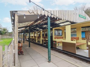 A small train station platform with a covered waiting area and an open passenger train at The Station Flat in St Newlyn East near Newquay