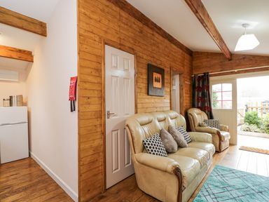 A living room with leather sofas and a wooden paneled wall at The Log Cabin in Bushton near Royal Wootton Bassett
