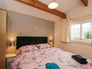 A bedroom with a double bed with floral pink bedding two bedside tables with lamps and a window with curtains at The Log Cabin in Bushton near Royal Wootton Bassett