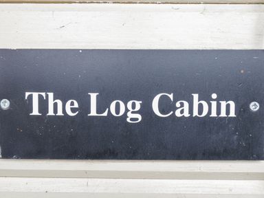 A black sign with white text reading The Log Cabin