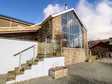 An exterior view of a stone building with large windows a staircase with glass railing and planters at The Barn at Glanoer Hundred House near Builth Wells