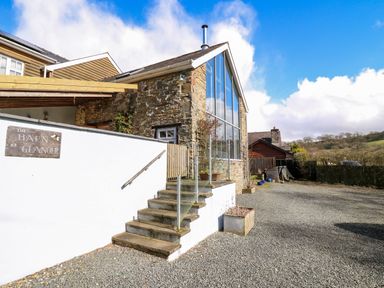 The exterior of a stone barn with large glass windows and steps leading to a white wall at The Barn at Glanoer Hundred House near Builth Wells