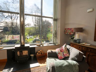 A living room with a wood stove and armchair near a large window at The Barn at Glanoer Hundred House near Builth Wells