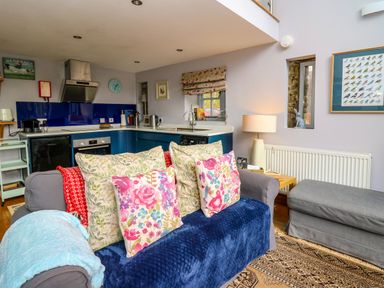 A living room with a sofa covered in cushions and a kitchen area in the background at The Barn at Glanoer in Hundred House near Builth Wells