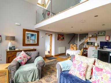 A living room with floral cushions on chairs and a small kitchen area at The Barn at Glanoer Hundred House near Builth Wells
