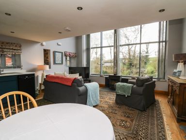 A living room with two sofas and a wood stove by large windows at The Barn at Glanoer Hundred House near Builth Wells