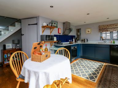 A kitchen with blue cabinets a round table with wooden chairs and a wicker basket on the table at The Barn at Glanoer Hundred House near Builth Wells