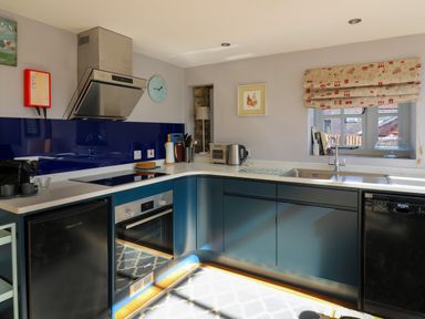 A kitchen with blue cabinets a sink stove oven coffee machine and a window with a patterned blind at The Barn at Glanoer Hundred House near Builth Wells