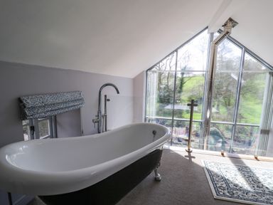 A bathroom with a freestanding bathtub and large triangular window with a view of trees and grass at The Barn at Glanoer Hundred House near Builth Wells