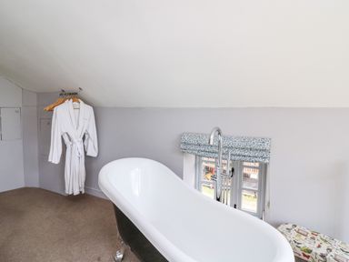 A bathroom with a freestanding bathtub a window with a floral blind a white bathrobe on hangers and a patterned cushioned seat at The Barn at Glanoer Hundred House near Builth Wells
