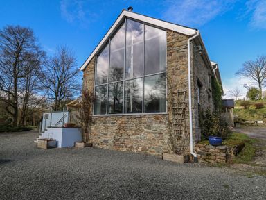 A stone building with large glass windows and gravel driveway at The Barn at Glanoer Hundred House near Builth Wells