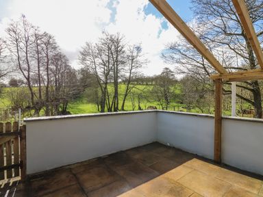An outdoor patio with tiled floor wooden gate and white walls overlooking green fields and trees at The Barn at Glanoer Hundred House near Builth Wells