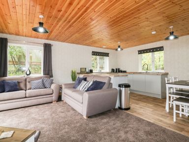 An open living room and kitchen with grey sofas and a dining table at Lodge One Brighton near Summercourt