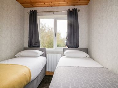 A bedroom with two single beds separated by a window with dark curtains at Lodge One Brighton near Summercourt