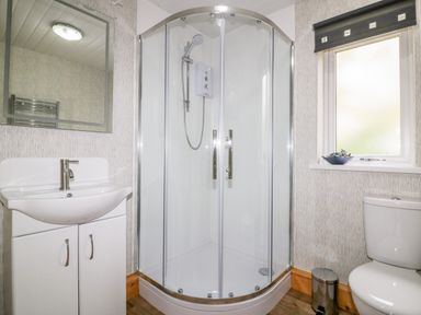 A bathroom with a shower enclosure a white sink with cabinet a toilet a window and a small trash bin at Lodge One Brighton near Summercourt
